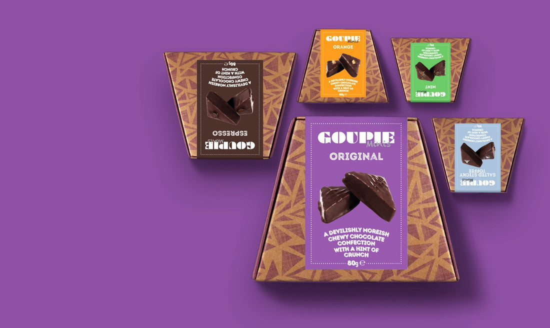 A purple image with images of all five Goupie mini flavours in their packaging. Original is large and at the front, around it are Espresso, Orange, Mint, and Salted Sticky Toffee Goupie boxes.