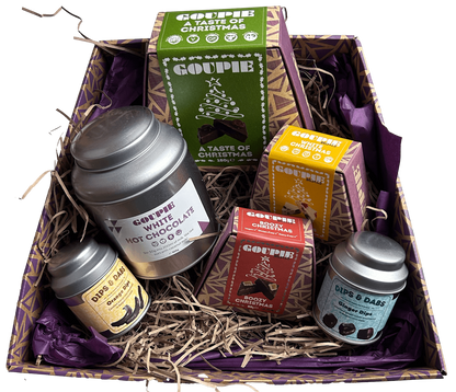 A vegan gift box filled with various Christmas themed snacks, including a hot chocolate tin and boxes of vegan chocolate