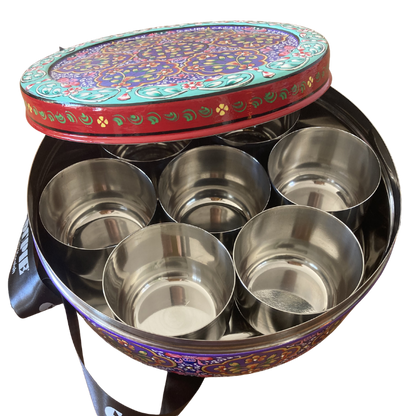 A round decorative gift tin with a colourful floral and paisley pattern, slightly opened to show 7 smaller internal tins