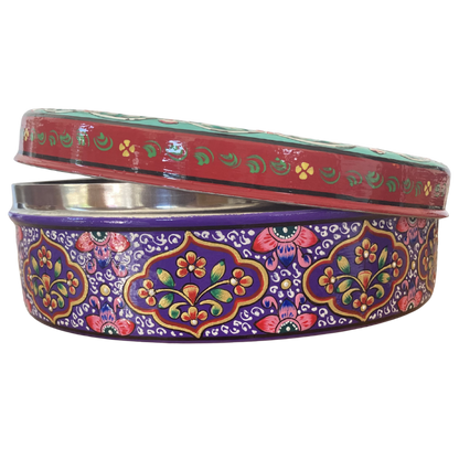 Sideview of a round decorative gift tin with a colourful floral and paisley pattern, slightly opened